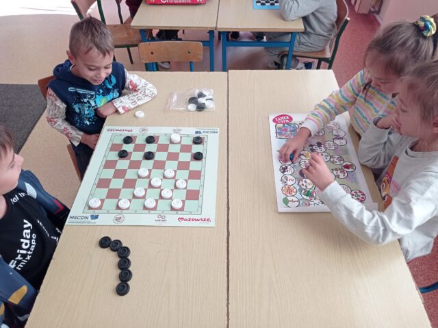 Chłopcy grają w  warcaby. Dziewczynki rywalizują w grze planszowej „Zamek cyfr”.
