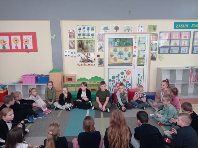 Zajęcia dydaktyczne: uczniowie siedzą na dywanie. Wychowawca prowadzi rozmowę kierowaną na temat znaczenia drzew w życiu człowieka.