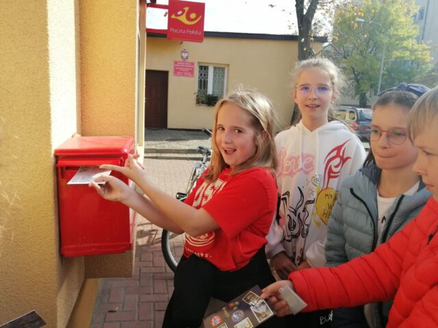 Zdjęcie 5-  Z uczniowskim pozdrowieniem - Ogólnopolska wymiana kartek pocztowych  społeczności szkół Jana Pawła II . Dzieci wrzucają pocztówki do skrzynki. 