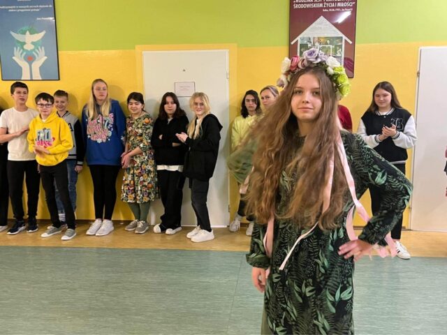 „Wiosenny pokaz mody” przygotowany przez uczennice klas szóstych i ósmych. Uczennica w wianuszku i zielonej sukience.