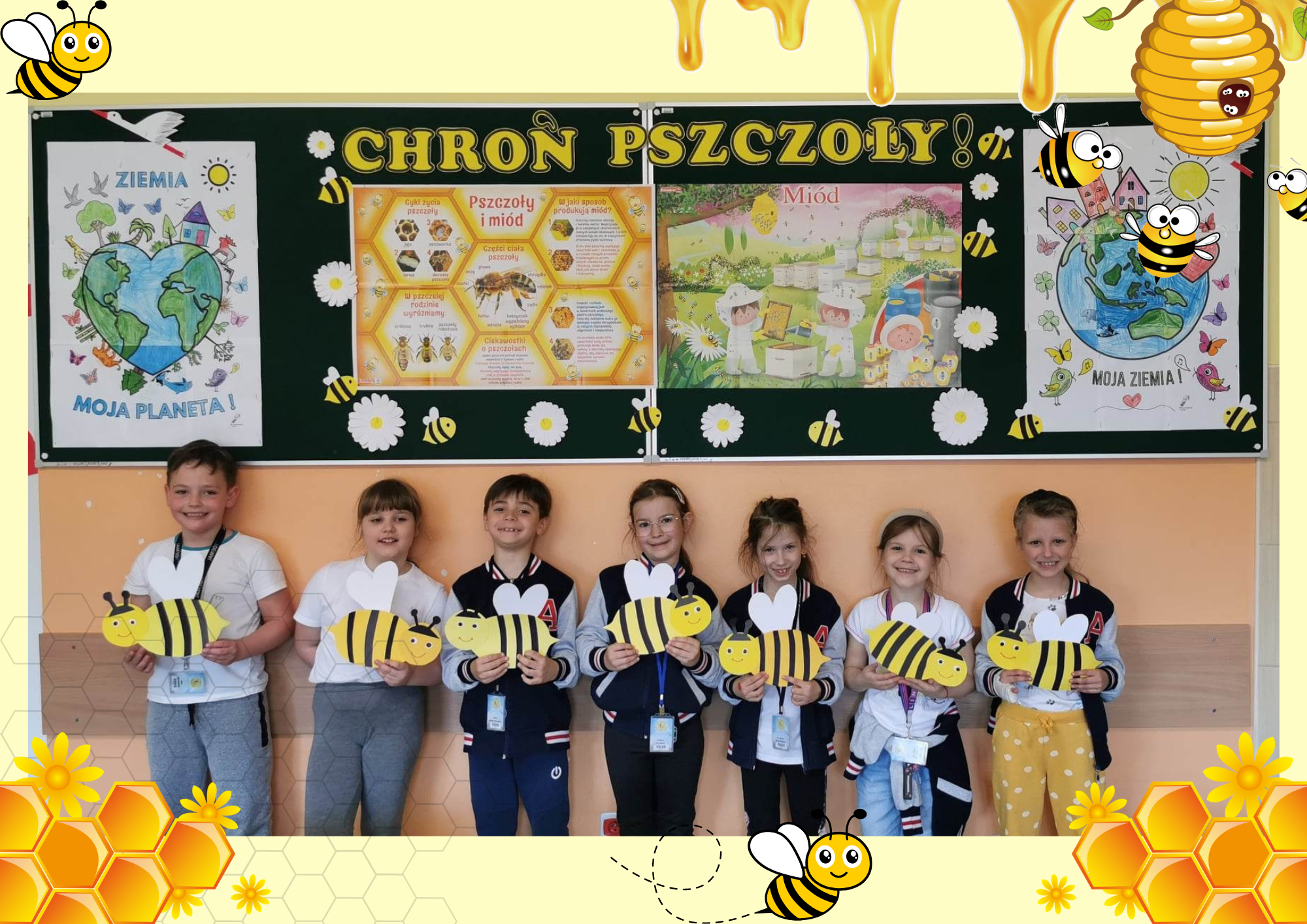 Zdjęcie grupowe. Uczniowie stoją na tle dekoracji tematycznej i pokazują samodzielnie zrobione z papieru pszczoły.